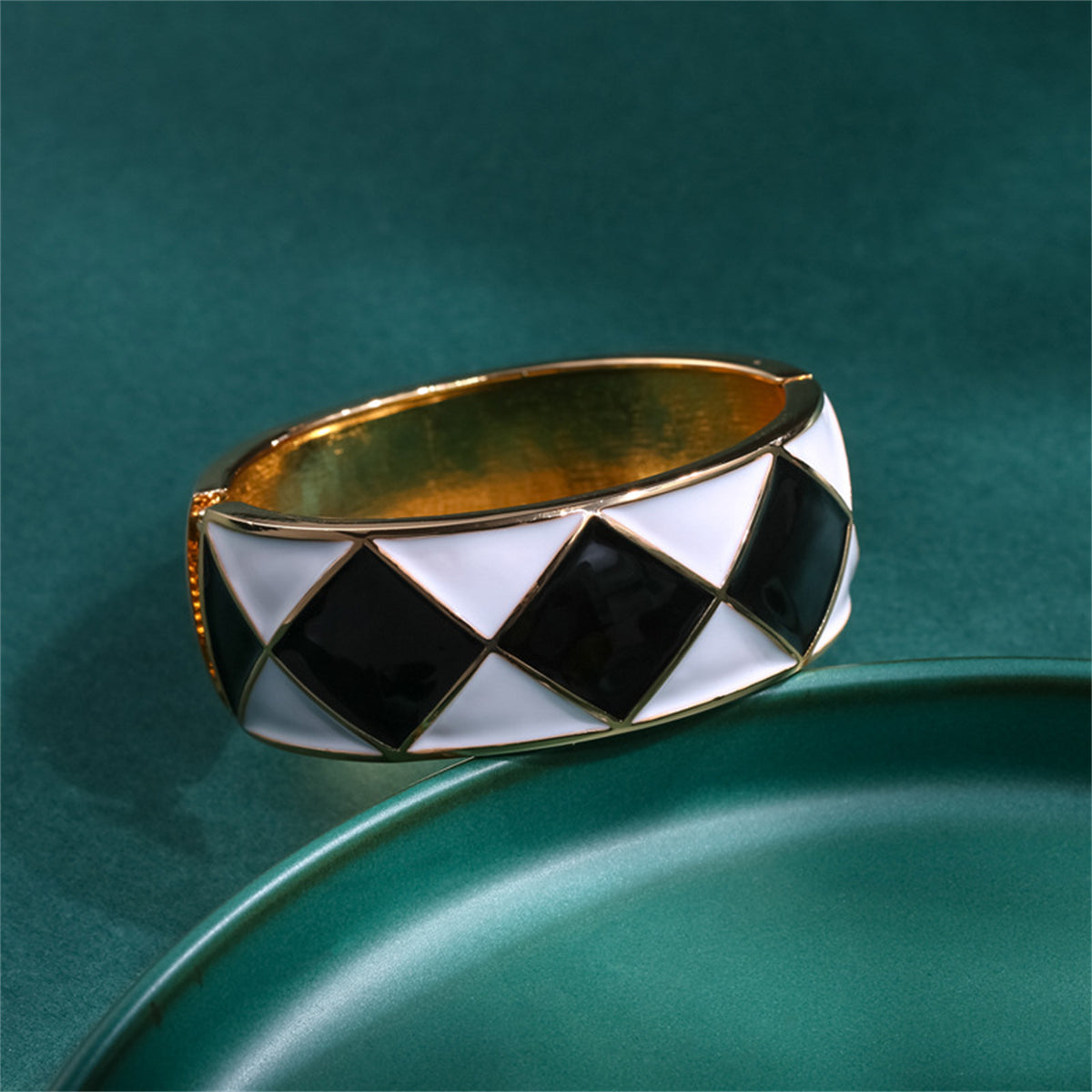 A sophisticated cuff bracelet featuring a black and white diamond pattern, made of black enamel and 18K gold-plated rhombus.