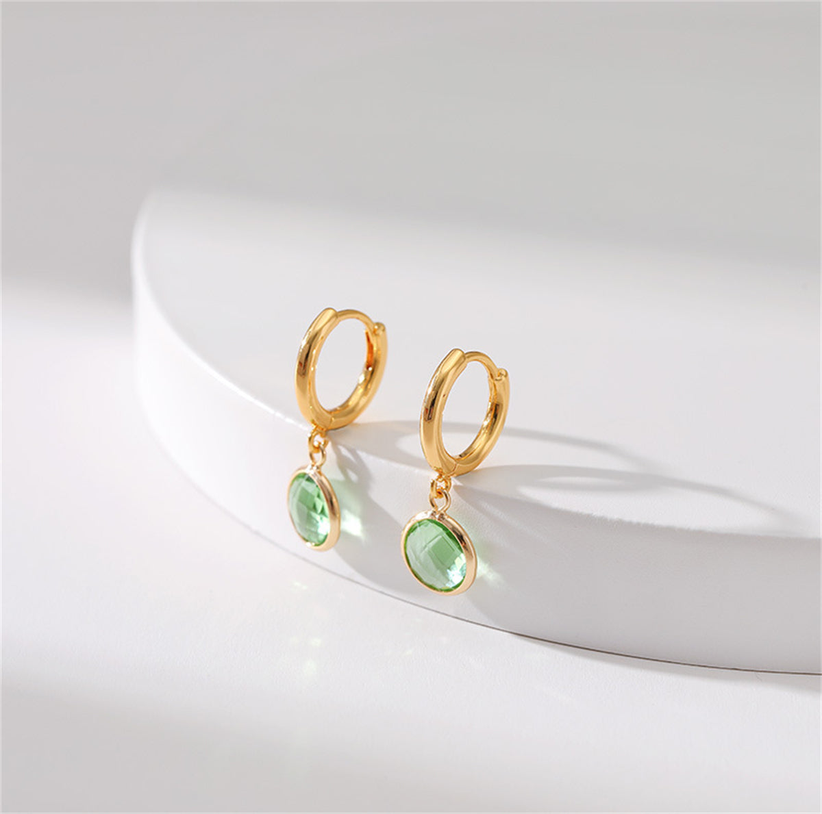 Elegant 18K gold-plated huggie earrings adorned with light green crystals, perfect for any occasion.