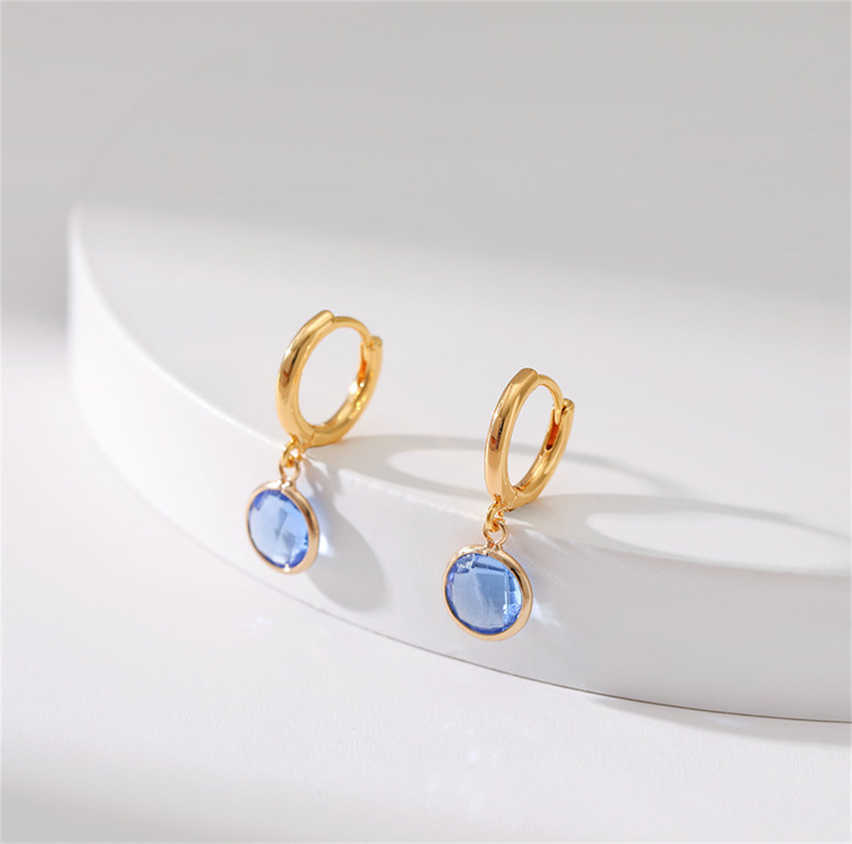 Stunning 18K gold-plated round huggie earrings adorned with blue topaz stones and purple crystals, showcasing exquisite craftsmanship.