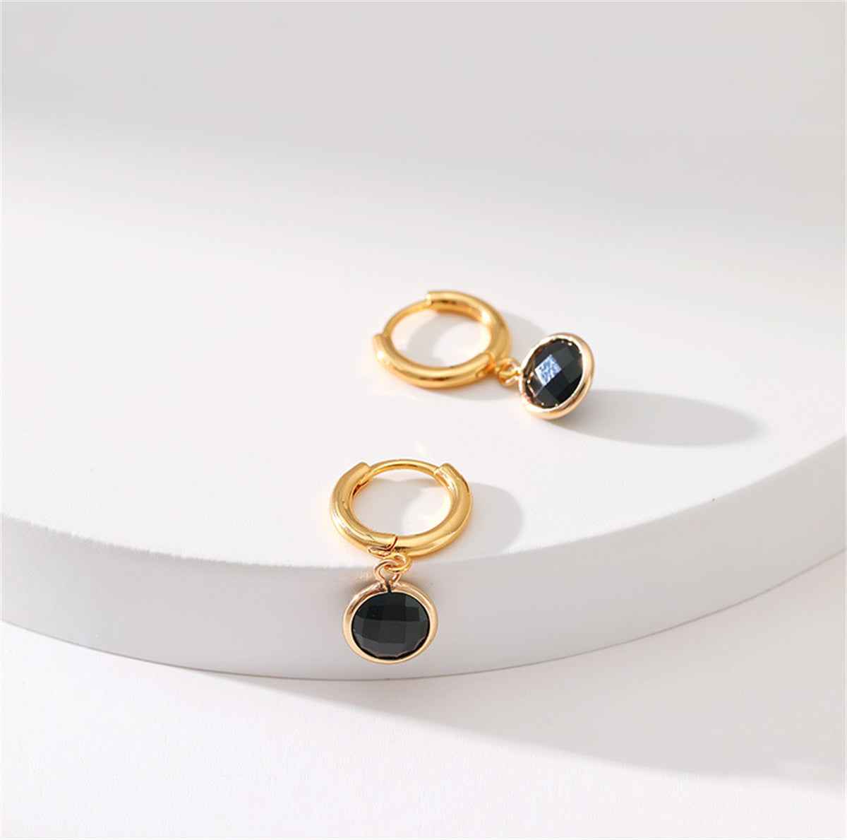 Black crystal round huggie earrings, elegantly plated in 18K gold, perfect for adding sophistication to any outfit.