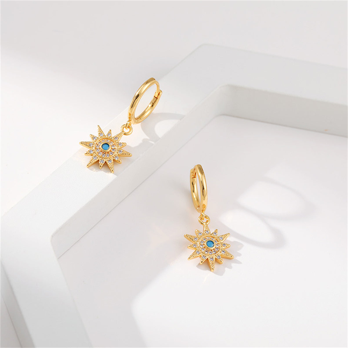 Chic gold-plated sun earrings with blue cubic zirconia stones, designed as huggies for a fashionable touch.