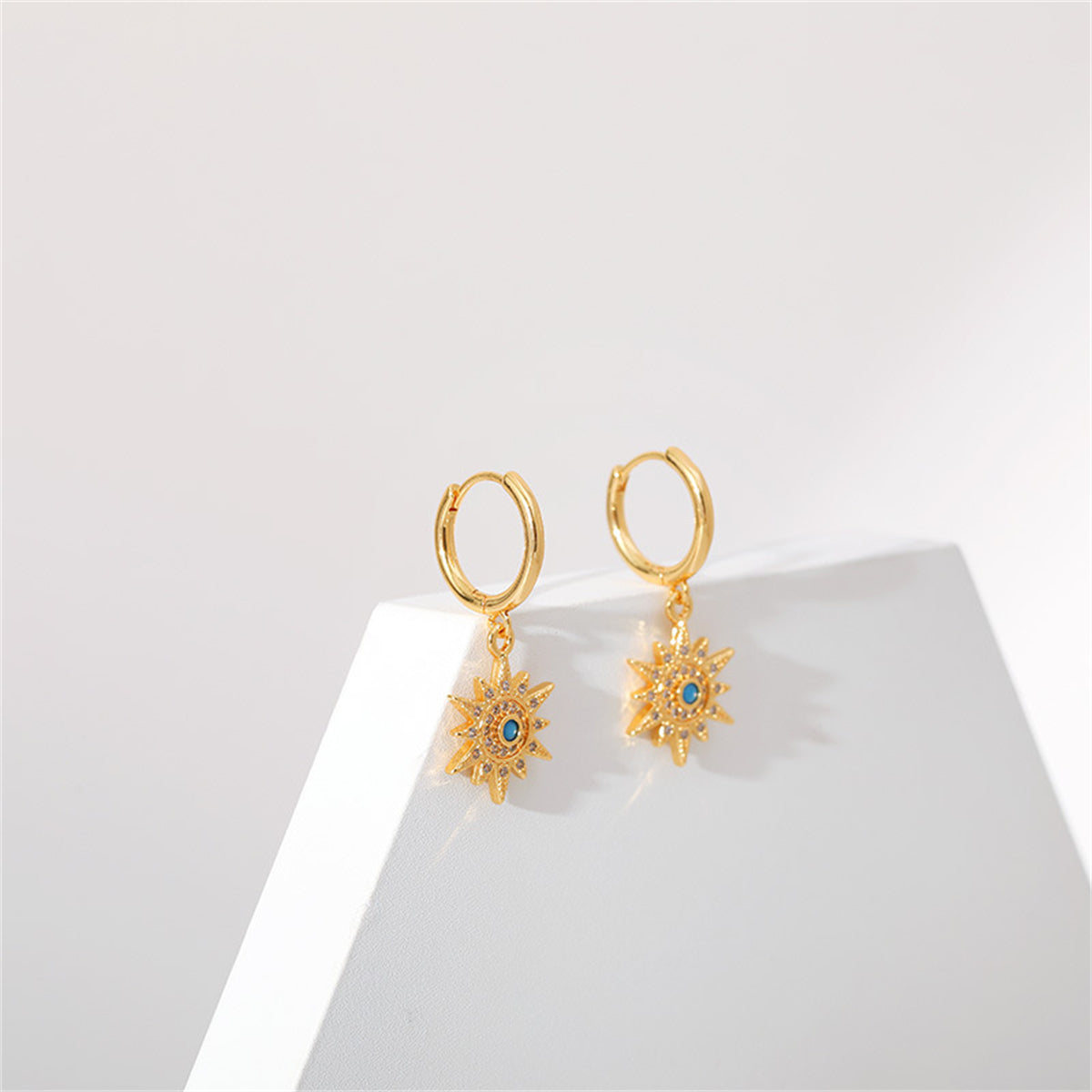 Stunning gold-plated sun earrings with blue cubic zirconia accents, designed as huggies for a chic appearance.